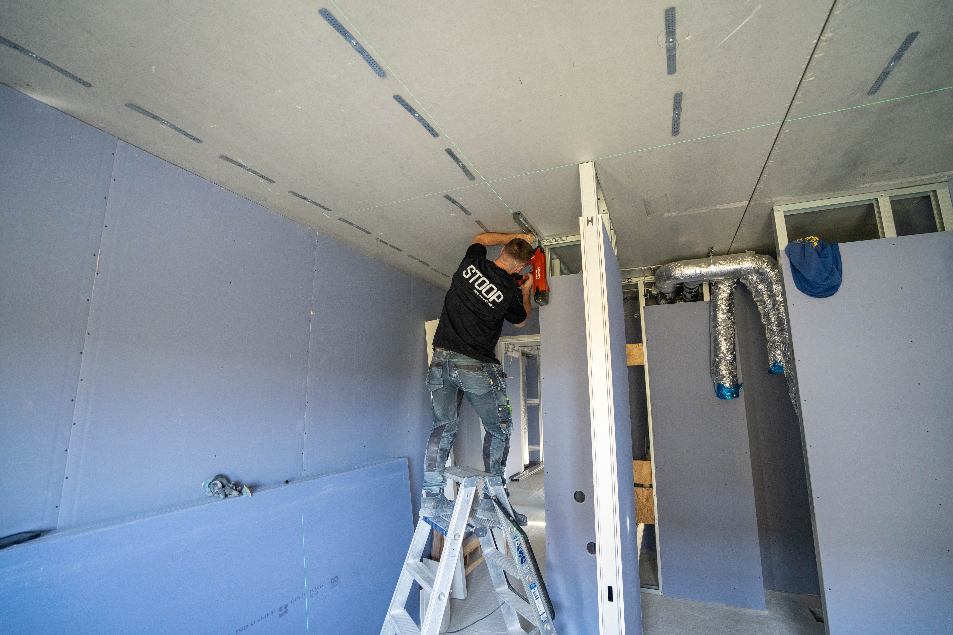 Medewerker van Stoop Aannemersbedrijf op een trap, aan het werk aan een plafond
