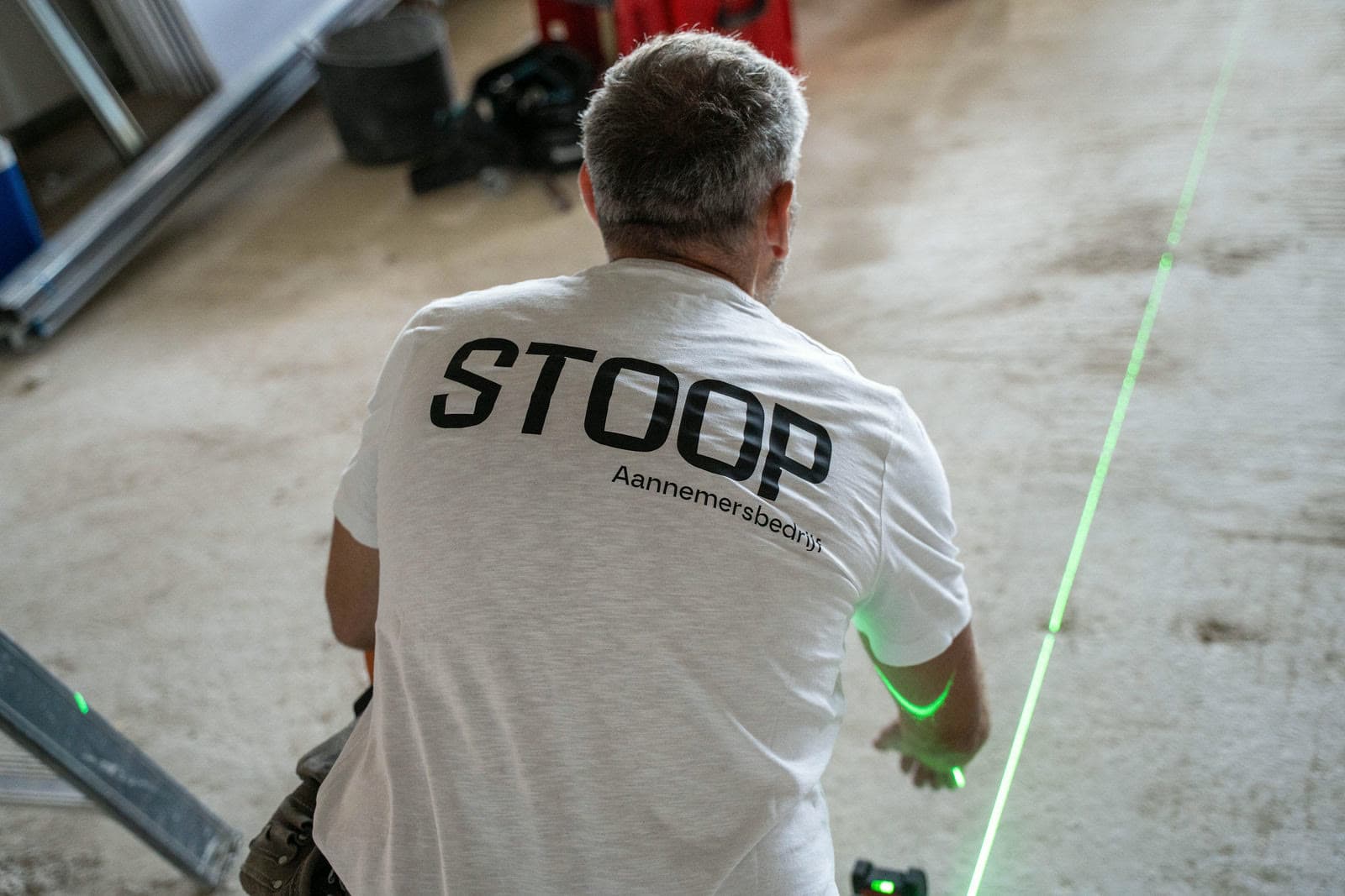 Medewerker van Stoop Aannemersbedrijf zet uit met een laserwaterpas, met het logo op de rug